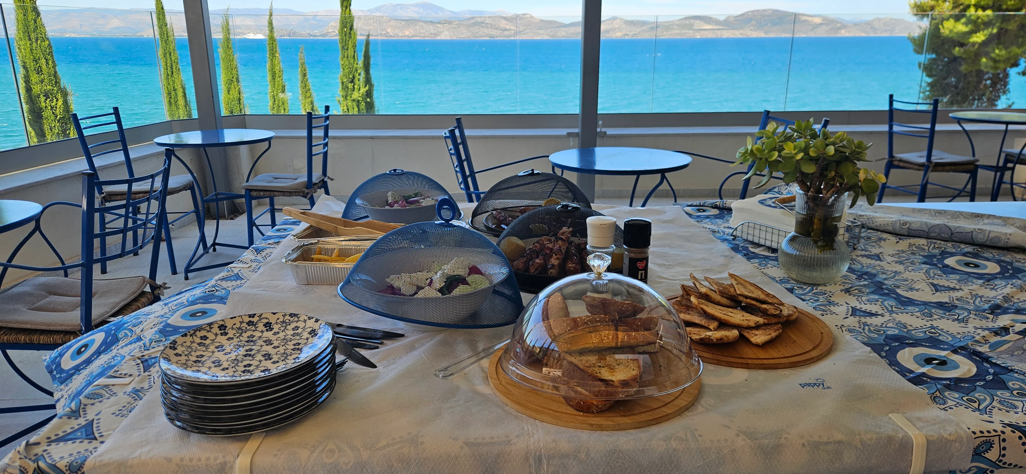 Τραπέζι πρωινού με σκεπασμένα πιάτα και θέα στον γαλάζιο κόλπο