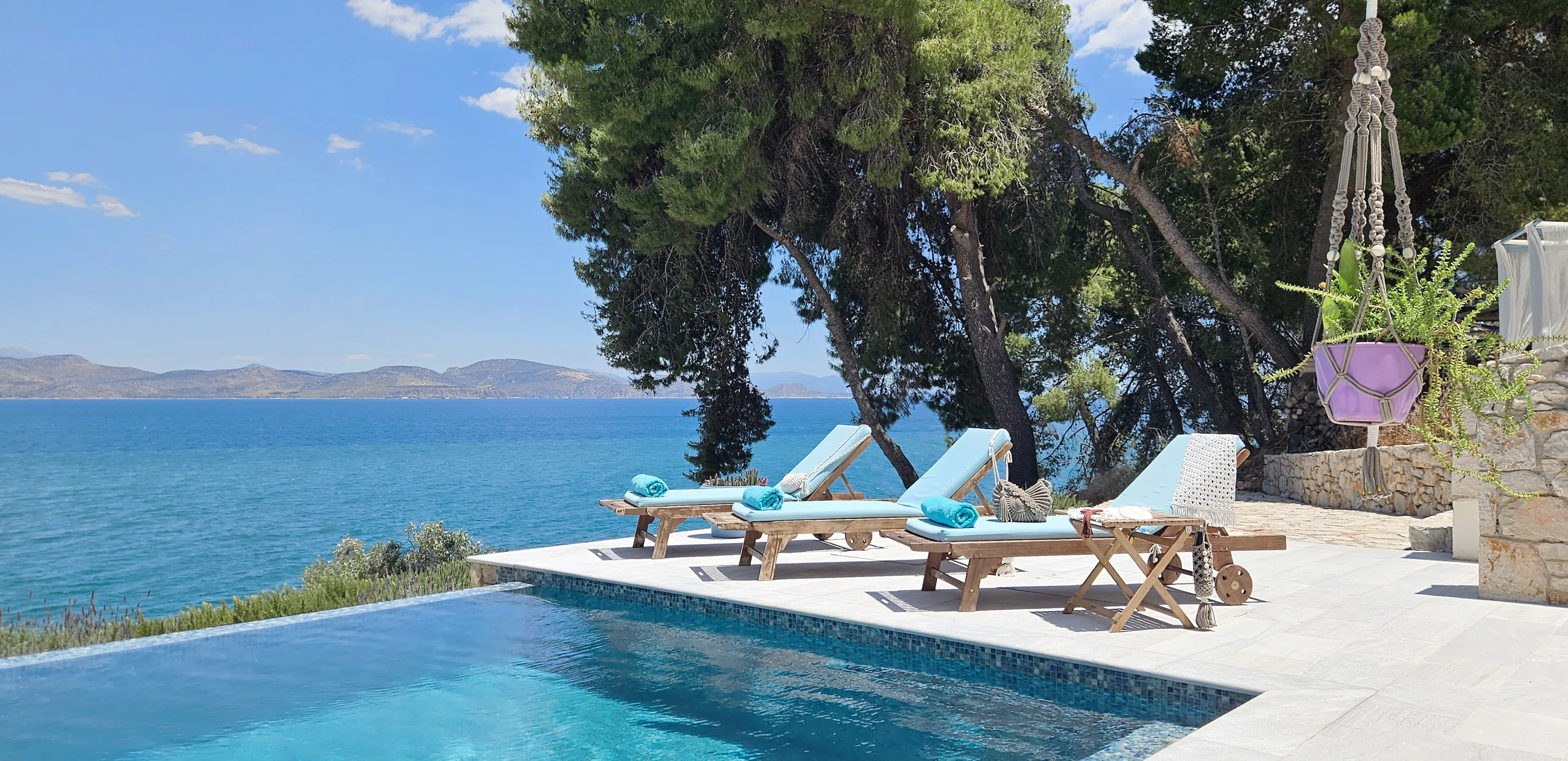 Liegen mit türkisfarbenen Auflagen am Pool unter den Pinien