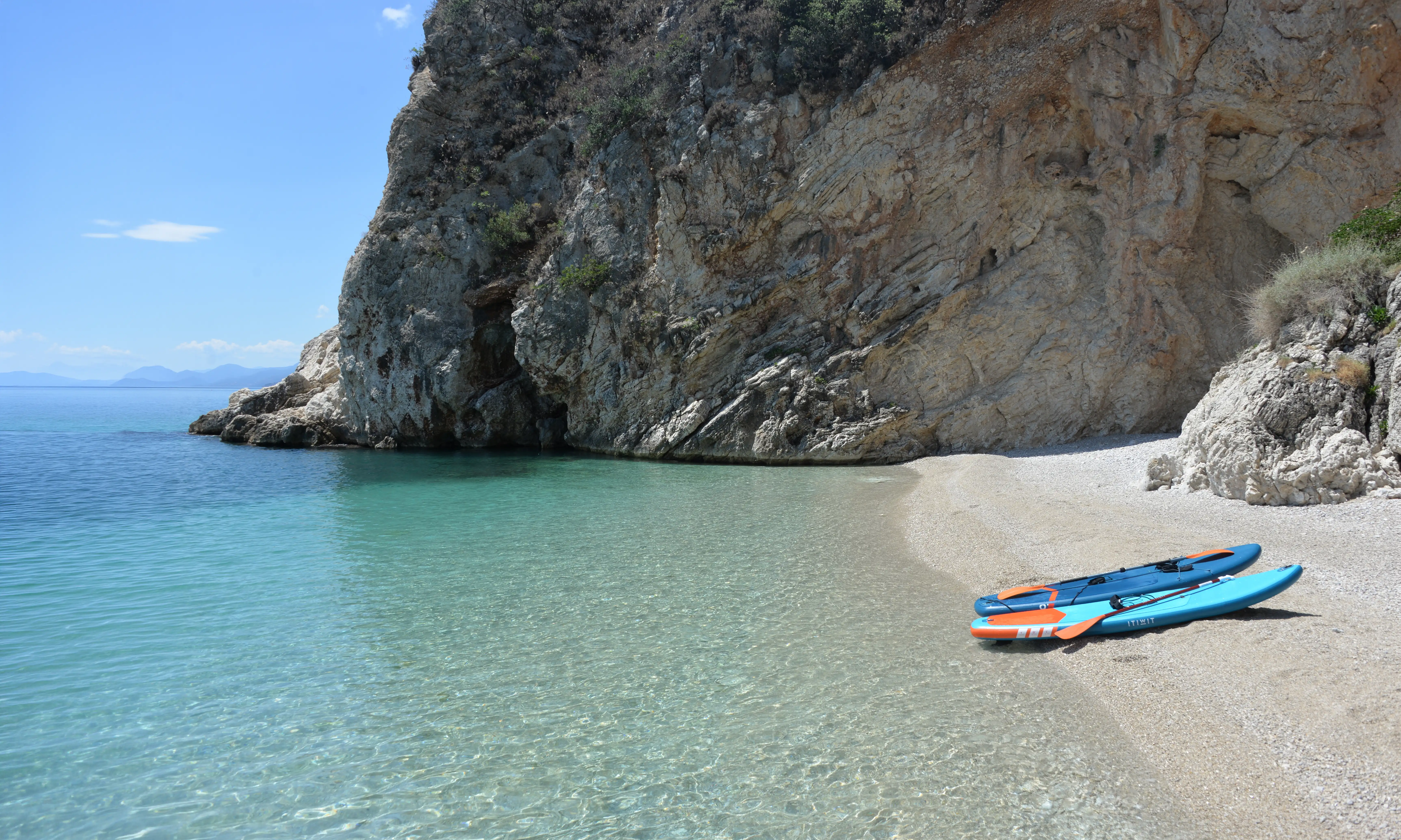 Kiesbucht mit klarem türkisfarbenem Wasser und zwei Paddleboards am Strand