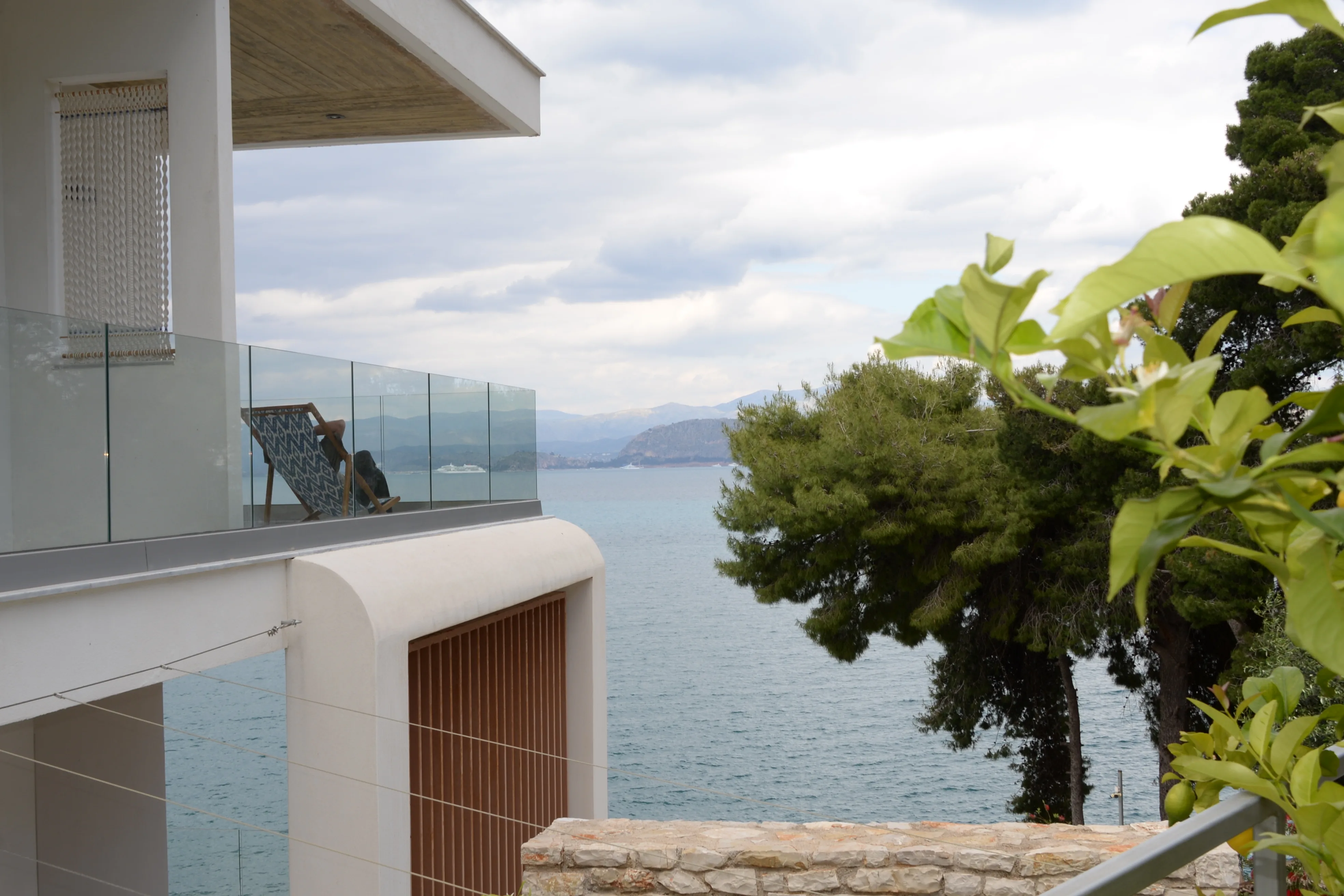 Balkon mit Glasbrüstung zwischen den Pinien, darunter das Meer