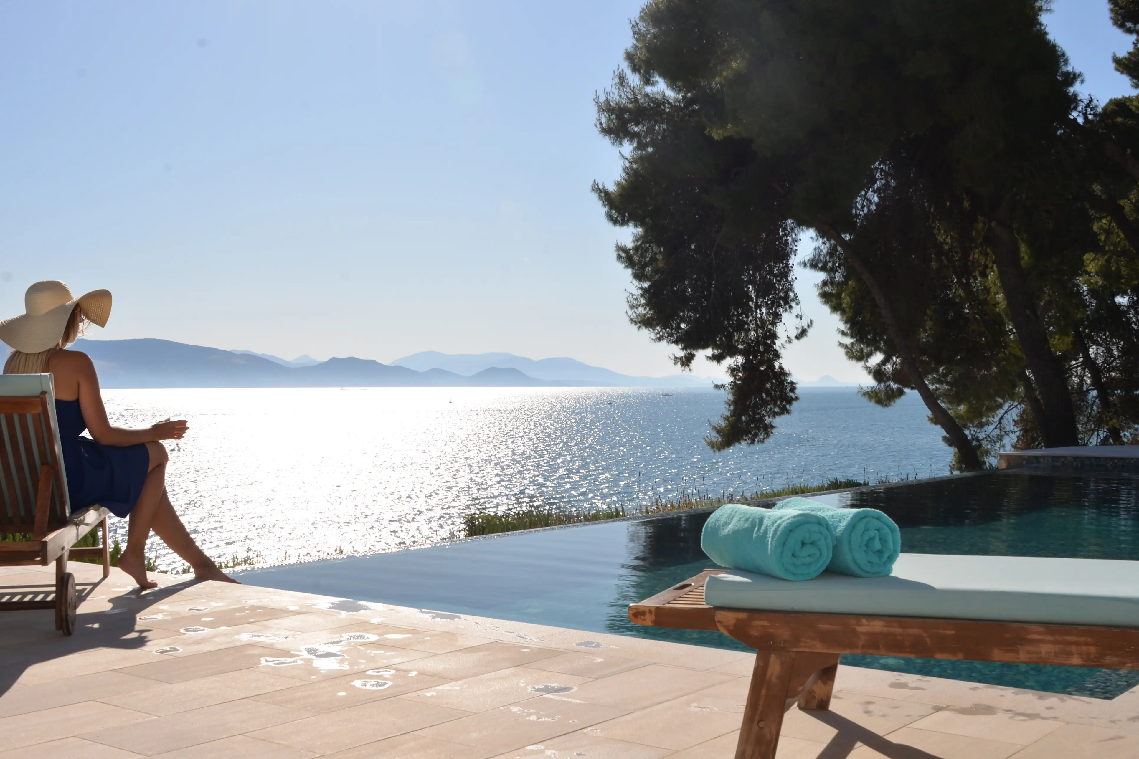 Gast mit Sonnenhut am Rand des Infinity-Pools mit Blick über den Argolischen Golf