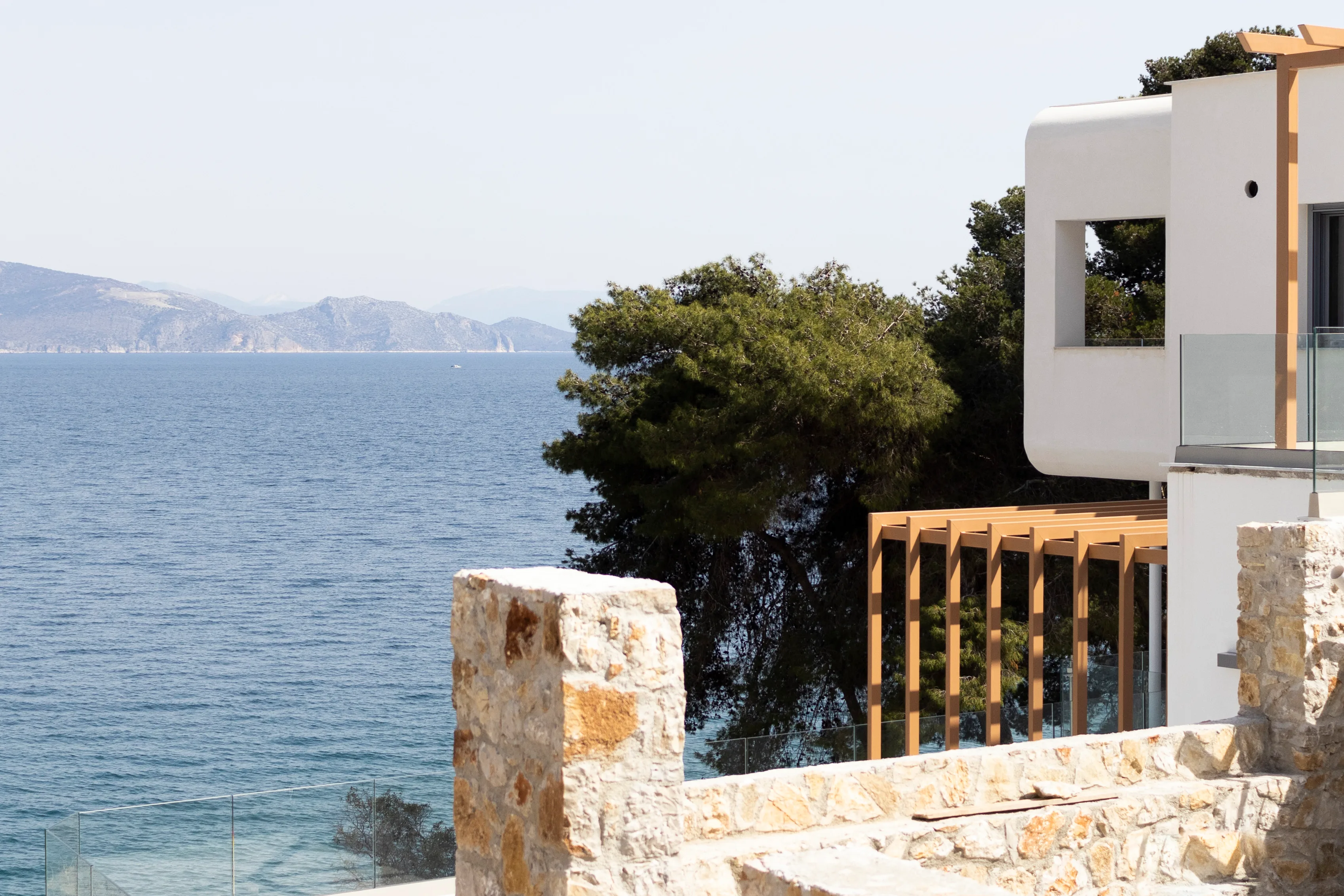 Weiße geschwungene Architektur, Holzpergola und Steinmauer über dem Meer