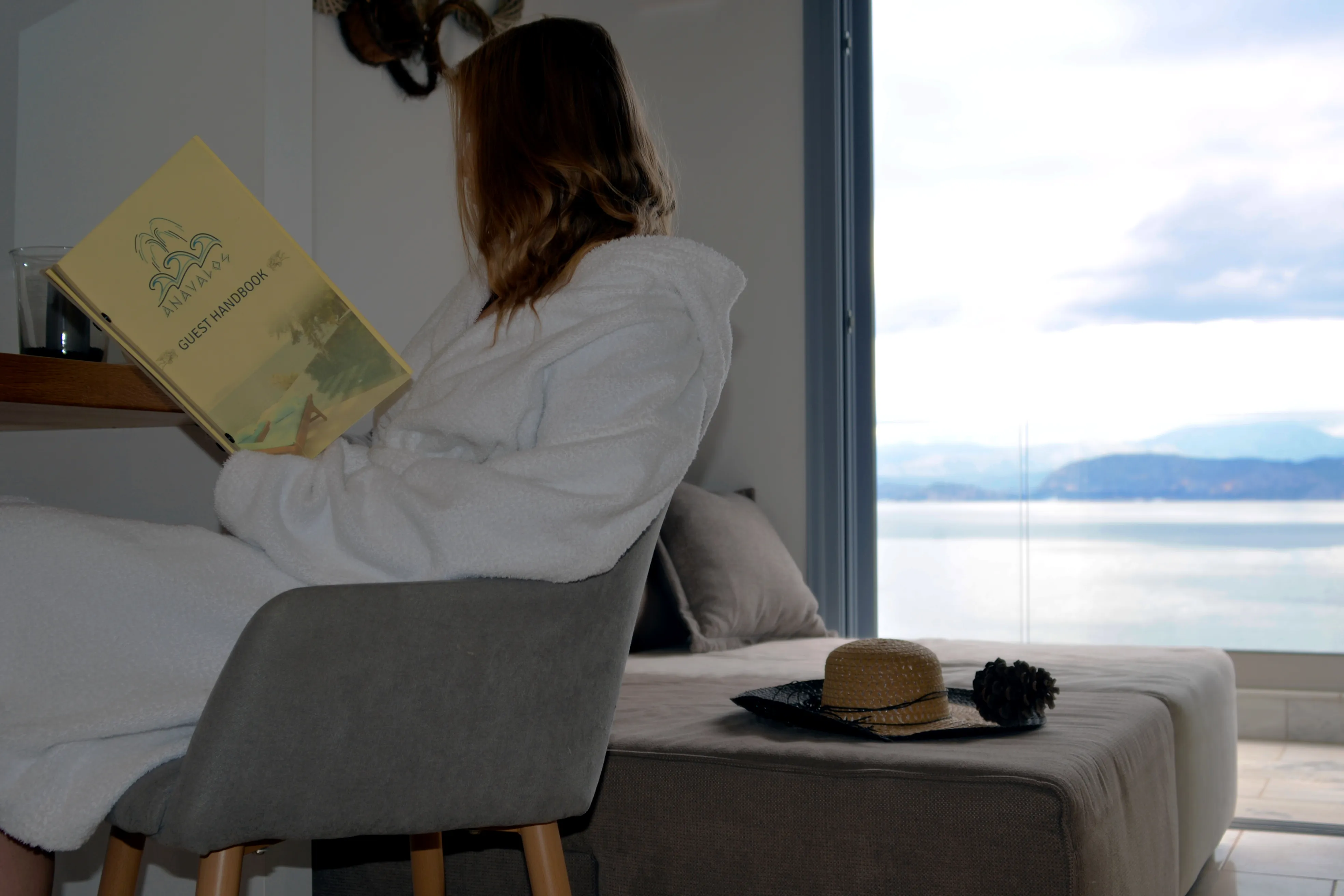 Gast liest im Sessel von Notos neben dem großen Fenster mit Meerblick